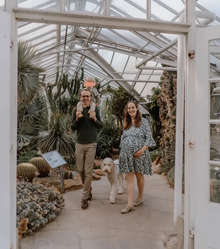 Familienshooting im botanischen Garten in Münster Paar mit Hund in einem Gewächshaus voller Pflanzen. Frau ist schwanger.