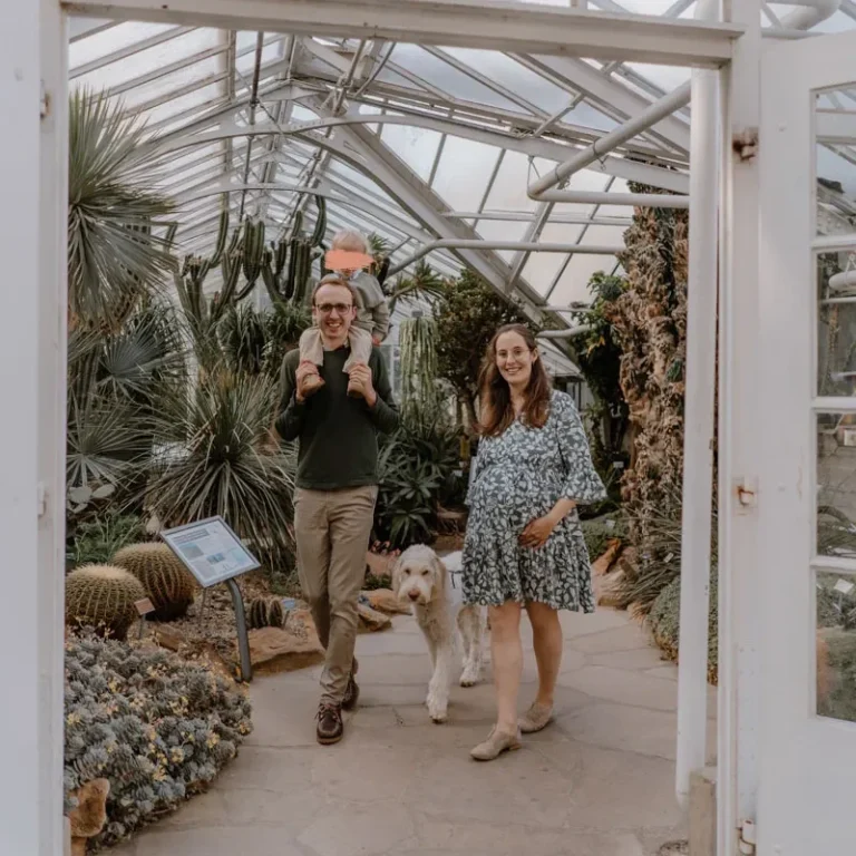 Familienshooting im botanischen Garten in Münster Paar mit Hund in einem Gewächshaus voller Pflanzen. Frau ist schwanger.